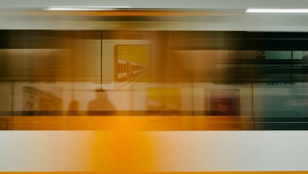 A white, yellow, and blue train rushes past the camera. It's therefore blurry from the speed.